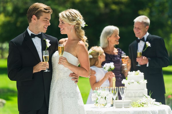 Married couple holding champagne flute, guests in background.