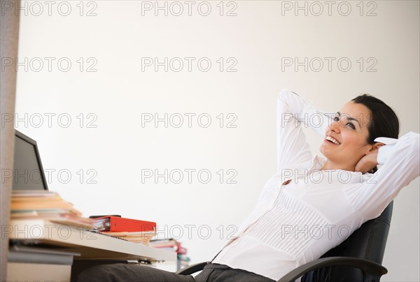 Businesswoman relaxing at desk in office. Photo : Jamie Grill