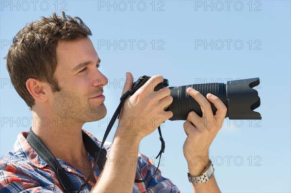 Man holding camera against blue sky.
