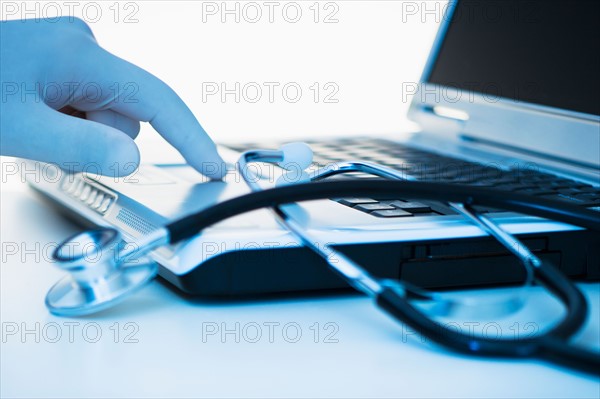 Studio shot of hand wearing surgical glove using laptop.