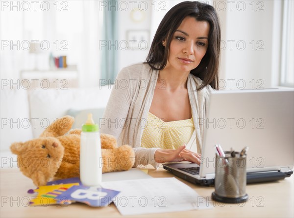 Working mother using laptop at home. Photo : Jamie Grill