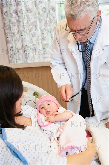 Doctor examining baby girl (2-5 months) held by mother.