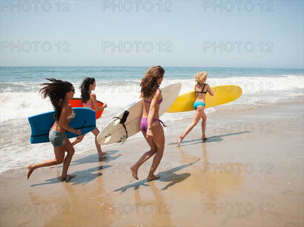 Group of young attractive women running into water with surfboards.
