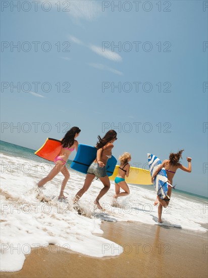 Group of young attractive women running into water with surfboards.
