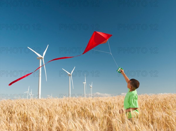 USA, Oregon, Wasco, Boy (8-9) playing with kite in wheat field, wind turbines in background. Photo: Erik Isakson