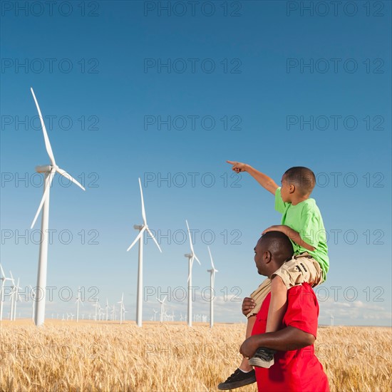 USA, Oregon, Wasco, Boy (8-9) piggy-back riding on father pointing at wind turbines. Photo: Erik Isakson