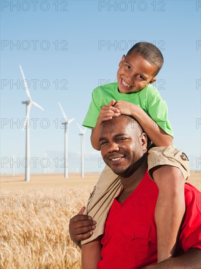 USA, Oregon, Wasco, Boy (8-9) piggy-back riding on father, wind turbines in background. Photo: Erik Isakson