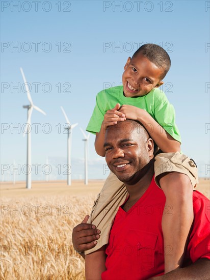 USA, Oregon, Wasco, Boy (8-9) piggy-back riding on father, wind turbines in background.