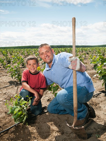 Father and son (8-9) planting trees in tree farm.