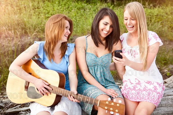 Three young women with guitar and cell phone relaxing. Photo: Take A Pix Media