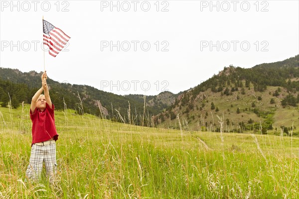 Boy (6-7) waving American flag in meadow. Photo: Shawn O'Connor