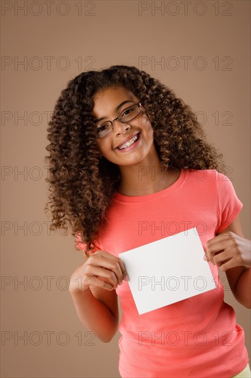 Studio portrait of girl (10-11) holding blank sheet of paper. Photo : Rob Lewine