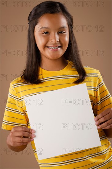 Studio portrait of girl (10-11) holding blank sheet of paper. Photo : Rob Lewine