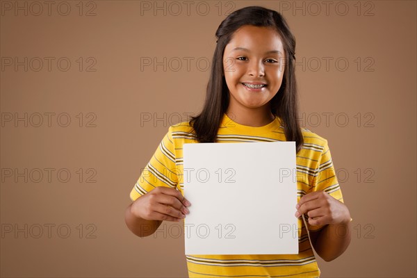 Studio portrait of girl (10-11) holding blank sheet of paper. Photo: Rob Lewine