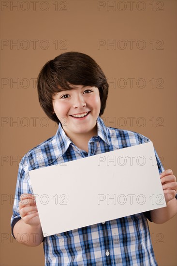 Studio portrait of boy (10-11) holding blank sheet of paper. Photo : Rob Lewine