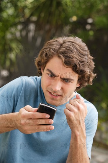 Young man text-messaging and shaking fist. Photo : Rob Lewine