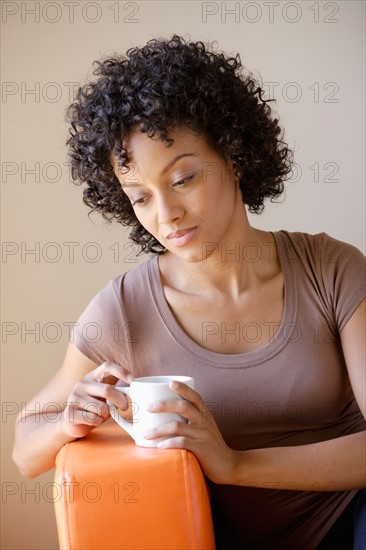 Young woman sitting in armchair holding cup. Photo : Rob Lewine