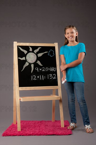Studio portrait of girl (8-9) standing next to blackboard. Photo: Rob Lewine