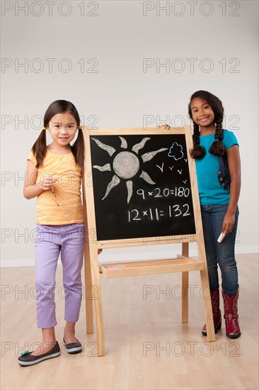 Studio portrait of two girls (8-9) standing by blackboard. Photo : Rob Lewine