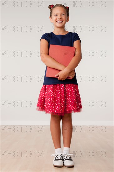 Studio portrait of girl (8-9) holding book. Photo : Rob Lewine