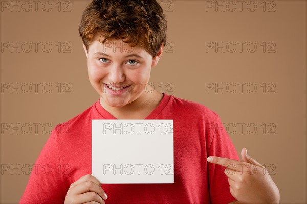 Studio portrait of boy (12-13) holding blank sheet of paper. Photo : Rob Lewine