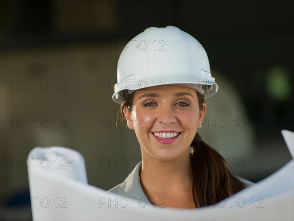 Portrait of woman wearing hardhat reading blueprint. Photo : db2stock