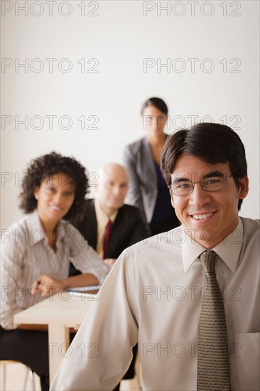 Smiling businessman looking at camera, business team in background. Photo : Rob Lewine