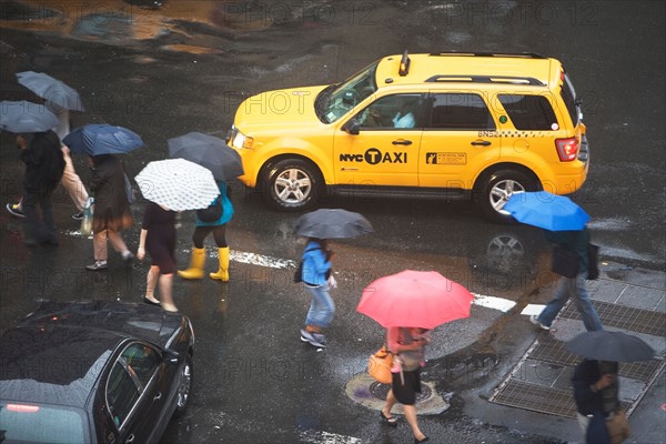 USA, New York State, New York City, Manhattan, Yellow taxi cab on street, pedestrians walking with umbrellas. Photo: fotog
