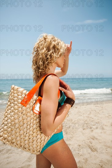 Young attractive woman carrying straw bag on sandy beach.