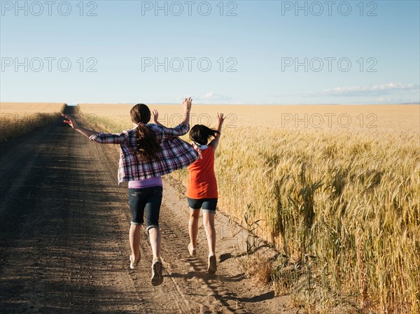 Girls (12-13, 10-11) running along dirt road.