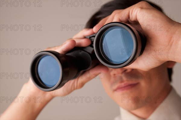 Businessman looking through binoculars. Photo : Rob Lewine