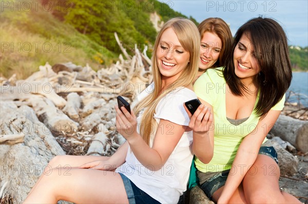Three young women hanging out on beach, using cell phones. Photo: Take A Pix Media