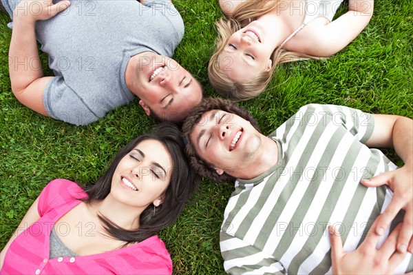 Four friends lying on grass with eyes closed. Photo: Take A Pix Media