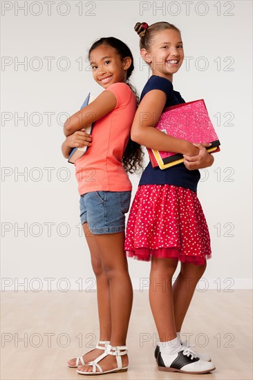 Studio portrait of two girls (8-9) holding books. Photo: Rob Lewine