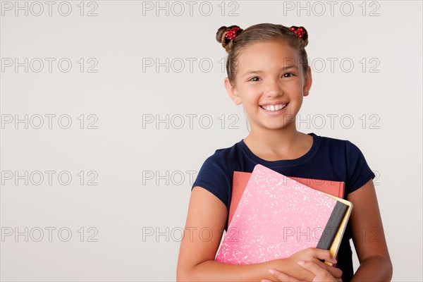 Studio portrait of girl (8-9) holding books. Photo : Rob Lewine