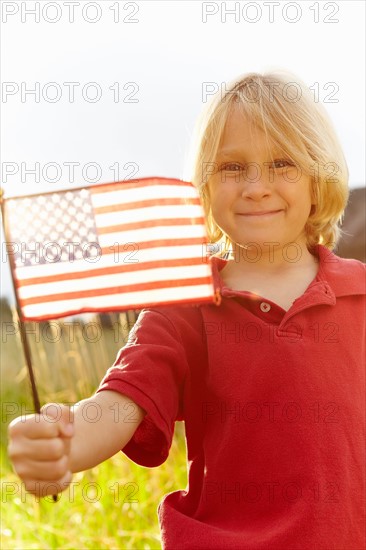 Portrait of boy (6-7) waving American flag in meadow. Photo: Shawn O'Connor