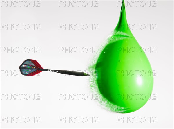 Studio shot of dart puncturing water-filled balloon.