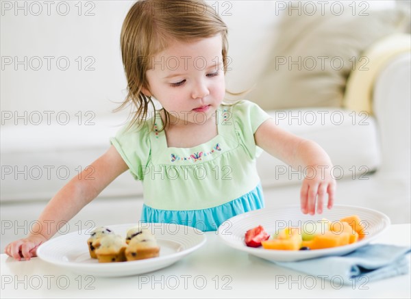 Girl (2-3) choosing between fruit salad and muffins.