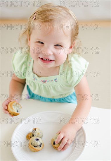 Girl (2-3) eating muffins.
