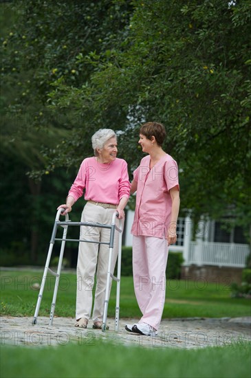 Senior woman walking with walker with help of nursing assistant.