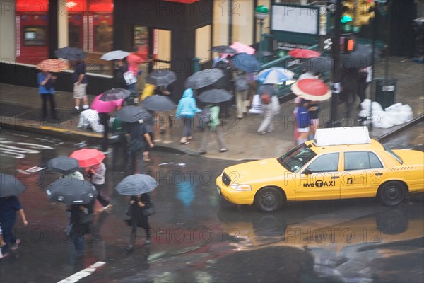 USA, New York State, New York City, Manhattan, Yellow taxi cab on street, pedestrians walking with umbrellas. Photo: fotog