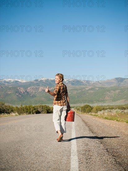 Mid adult woman carrying empty canister attempting to stop vehicles for help.