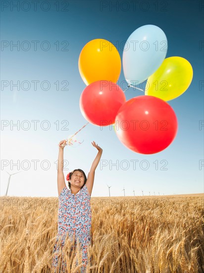 Happy girl (10-11) standing with balloons in wheat field.