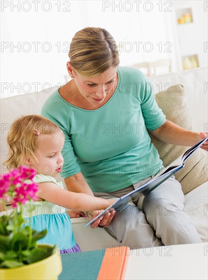 Mother with daughter (2-3) reading book on sofa.