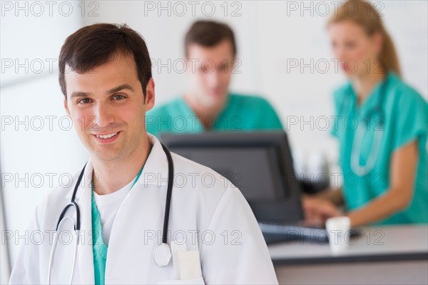 Portrait of male doctor in front of nurse's station.