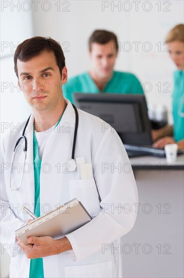 Portrait of male doctor in front of nurse's station.