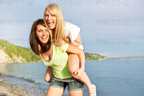 Portrait of two young women piggy-backing on beach. Photo : Take A Pix Media