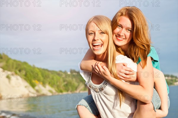 Portrait of two young women piggy-backing on beach. Photo : Take A Pix Media