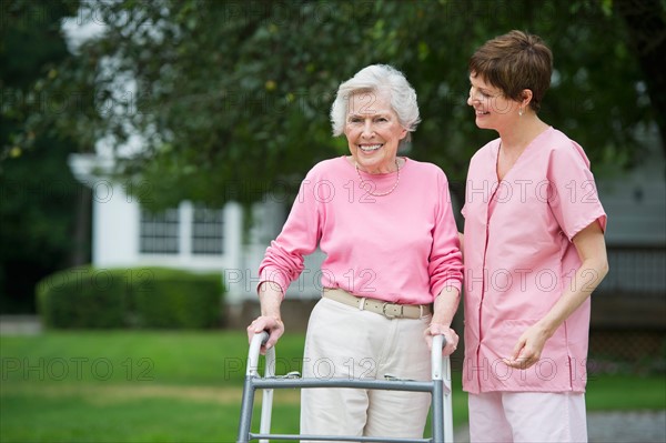 Senior woman walking with walker with help of nursing assistant.