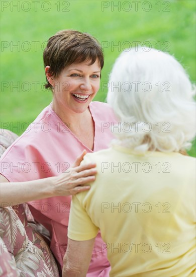 Senior woman and nursing assistant relaxing on outdoor sofa.